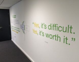 Wall graphic with a quote: "Yes, it’s difficult. Yes, it’s worth it." attributed to Forrest, in green and yellow text on a white wall.