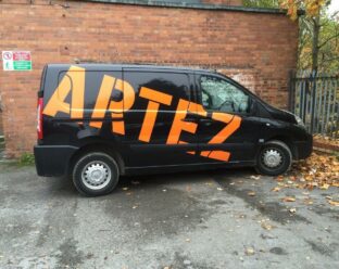 Black van parked on a street with the word "ARTEZ" in large, bold, orange letters across the side, partially obscured.