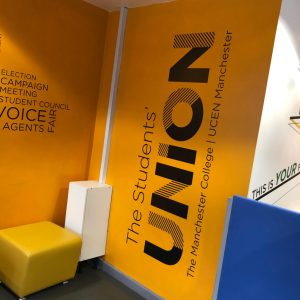 Wall graphic with the text: "The Students' UNION" and "The Manchester College | UCEN Manchester" on a bright yellow background.