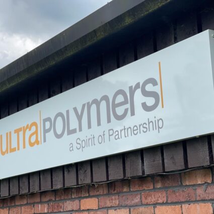 A large industrial building exterior featuring a white sign with the logo "ultra POLYMERS" and the tagline "a Spirit of Partnership" mounted on a dark wooden wall.