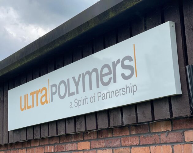 A large industrial building exterior featuring a white sign with the logo "ultra POLYMERS" and the tagline "a Spirit of Partnership" mounted on a dark wooden wall.