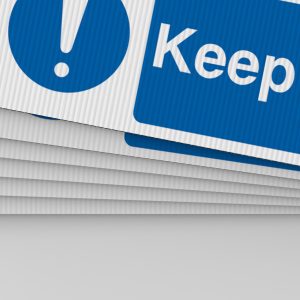 A close-up of several stacked Correx boards with a blue and white safety sign partially visible on the top sheet.