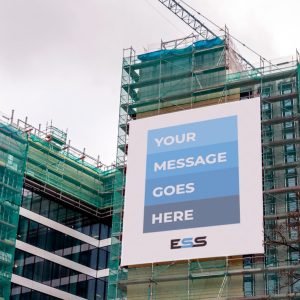A tall building under construction with a large scaffold banner displaying "YOUR MESSAGE GOES HERE" in blue shades, mounted on the scaffolding against a cloudy sky.