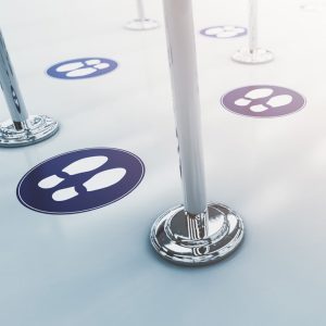 Floor with circular social distancing markers and metallic stanchions, showing printed floor graphics with footprints.