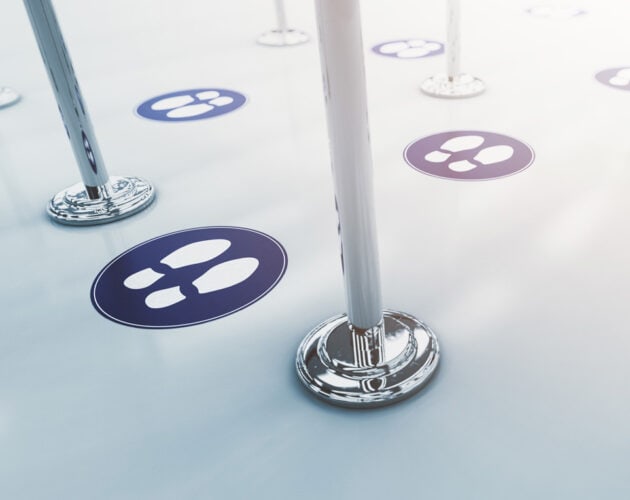Floor with circular social distancing markers and metallic stanchions, showing printed floor graphics with footprints.