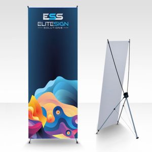 An X banner stand displaying a vibrant design with the "ESS Elite Sign Solutions" logo at the top and colorful abstract graphics below, positioned next to a plain white display board on a grey background.