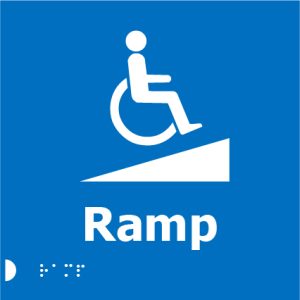 A blue square sign with a white wheelchair symbol on an inclined ramp, the word "Ramp" in bold white letters below, and Braille dots beneath.
