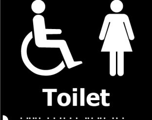 A black square sign with white icons of a person in a wheelchair and a woman, with the word "Toilet" in bold white letters below, and Braille dots beneath.