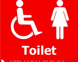 A red square sign displaying white icons of a person in a wheelchair and a woman, with the word "Toilet" in bold white letters below, and Braille dots beneath.