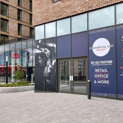 A row of commercial hoarding signs on a glass-fronted building, displaying contact information and advertisements for office, retail, and gym spaces, with a background of modern urban architecture.