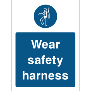 Warning sign with a blue background, white text “Wear safety harness,” and an icon of a person wearing a safety harness at the top