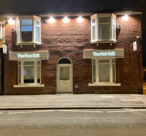Night-time photograph of a brick building with two illuminated shop signs reading “The Face Edit” and “The Hair Edit,” with bright exterior lights shining above.